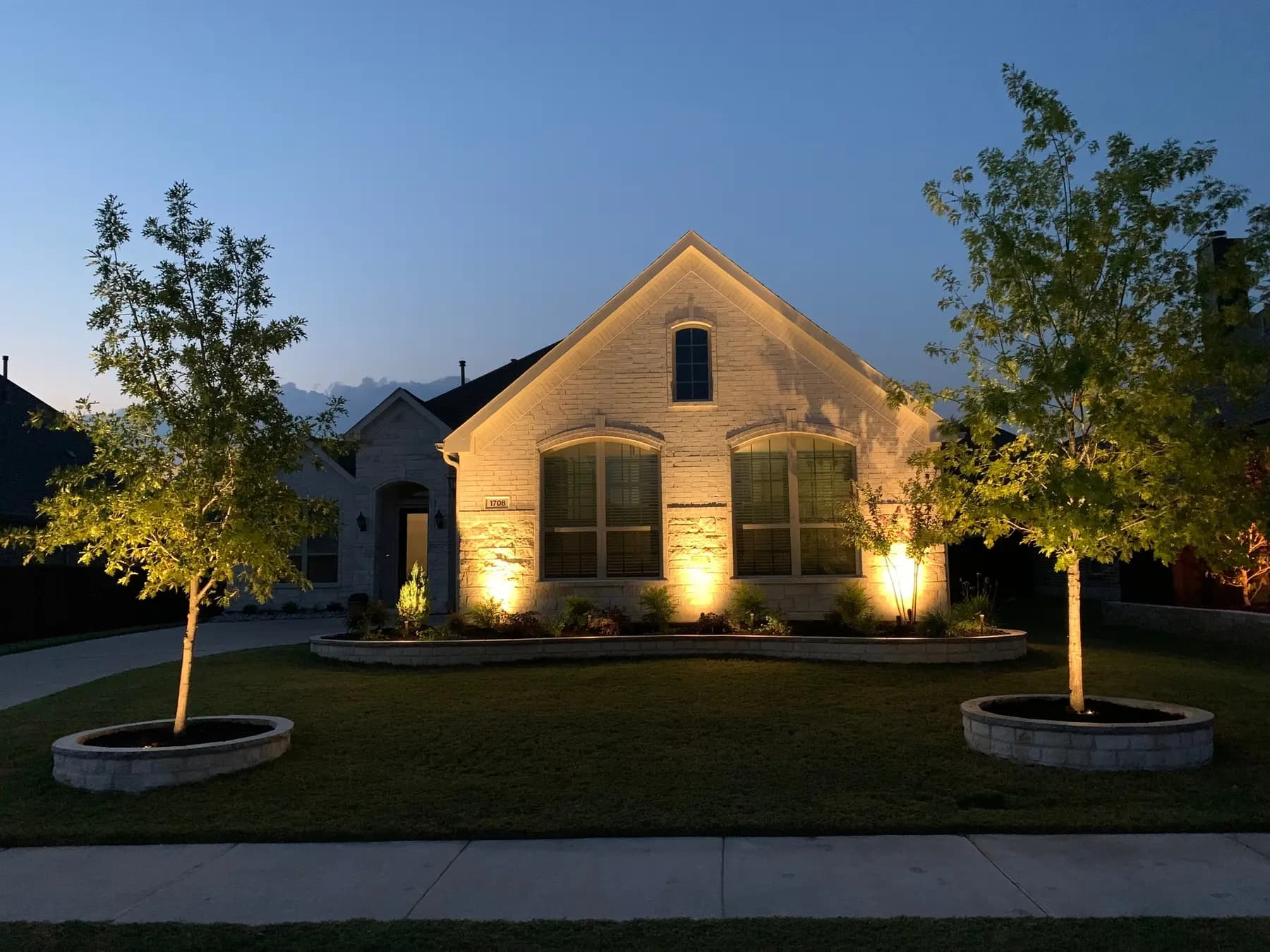 Warm landscape uplighting installed at a North Texas brick home